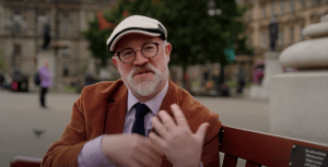 Niall Murphy sitting on a bench in George Square, Glasgow, speaking animatedly during an interview.