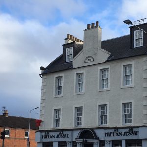 Street view of the Hielan Jessie pub, a white three-storey historic building with tall chimneys and symmetrical sash windows. The building features a pediment dated 1771 and stands against a partly cloudy blue sky.