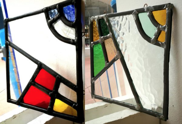 Two pieces of stained glass art with a black leaded outline and primary coloured geometric shapes