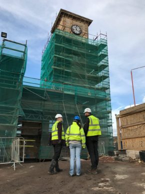 Three people wearing high viz jackets stand in front of a building covered in scaffolding